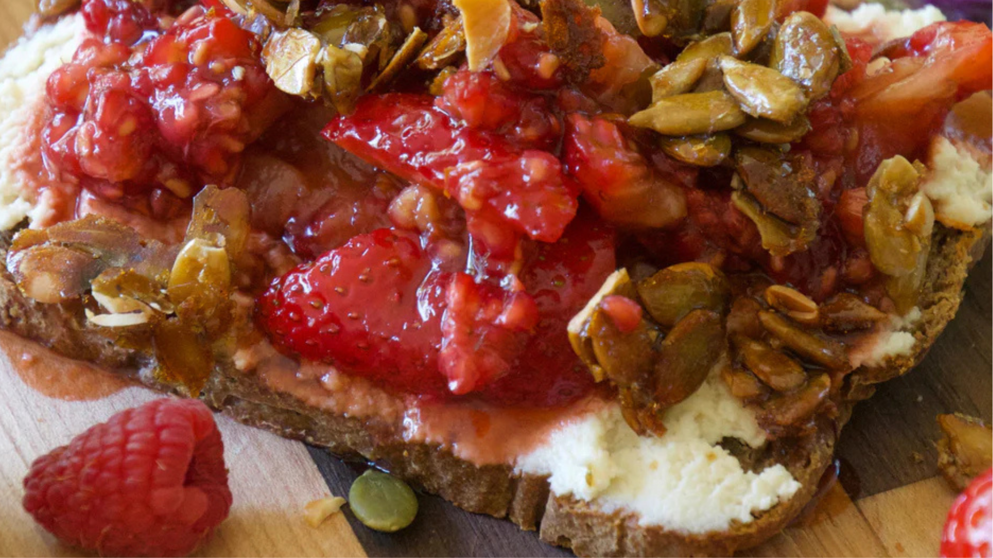 Close up of berry toast topped with sliced strawberries and pumpkin seeds on crusty bread
