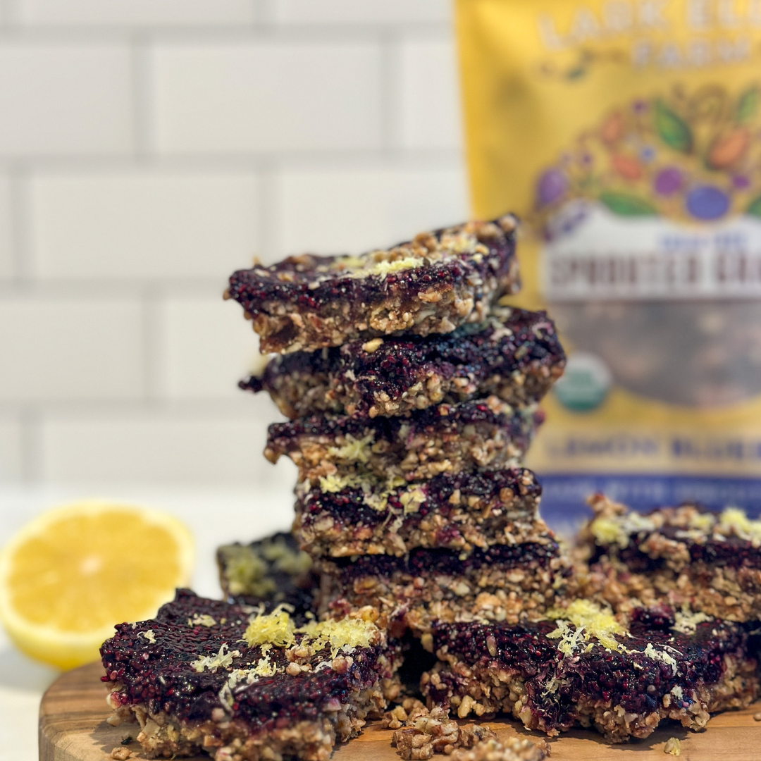 Lemon blueberry bars with an oat crust and lemon zest, stacked on a wooden board with a lemon half in the background