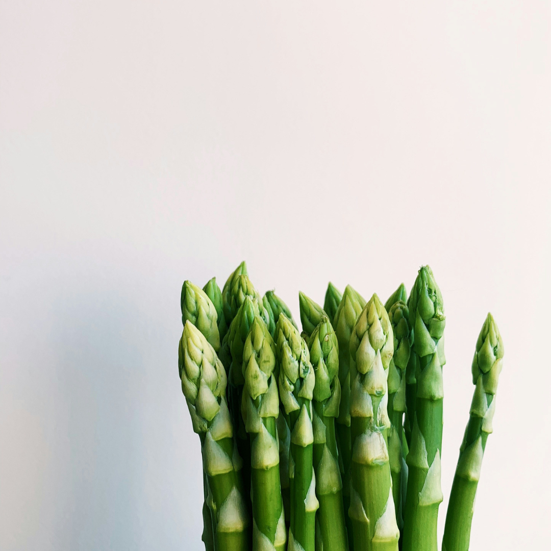 Bright green asparagus spears standing upright against a pale white background