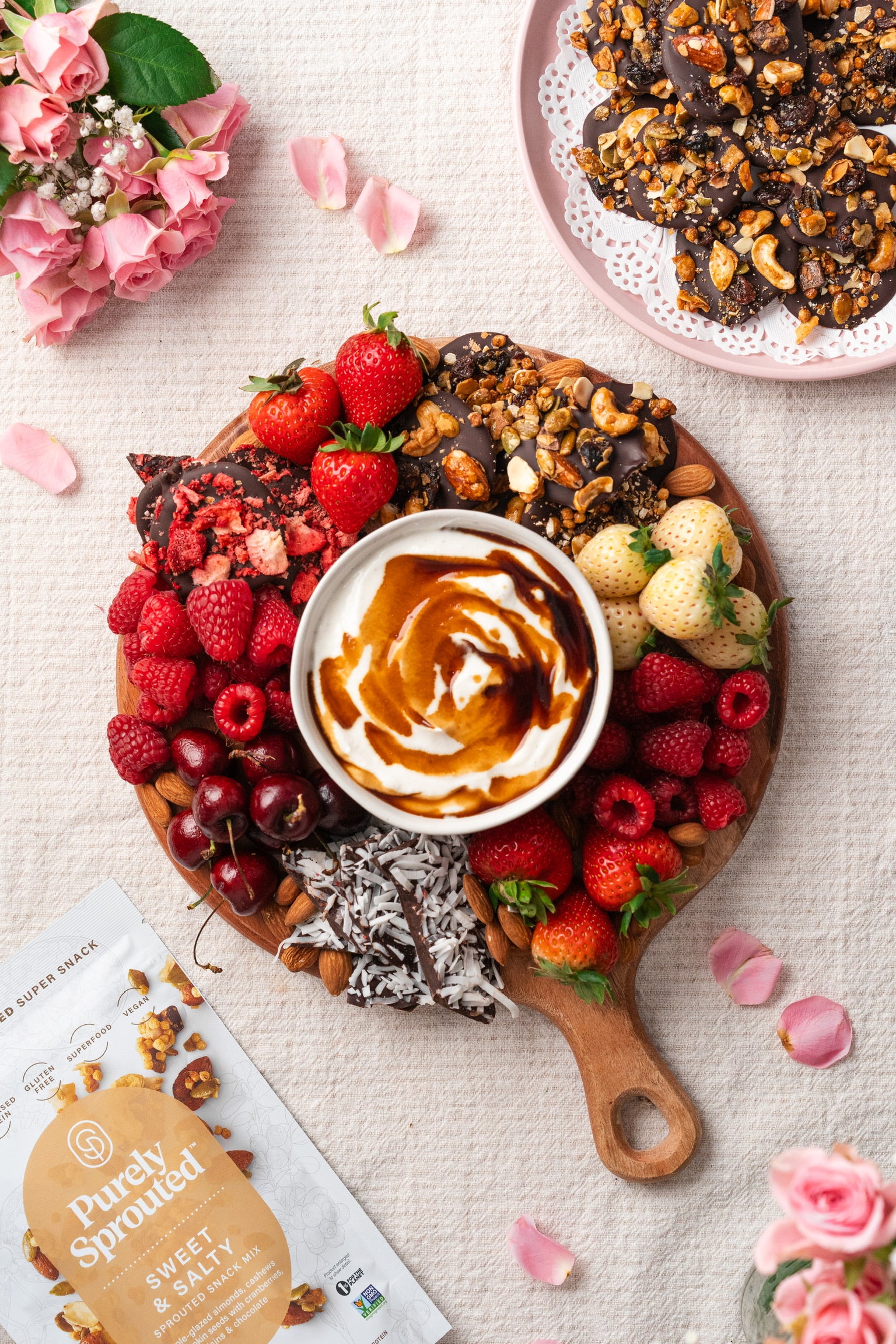Top view of a fruit and chocolate platter with mixed berries and a Purely Sprouted Sweet & Salty bag in the corner