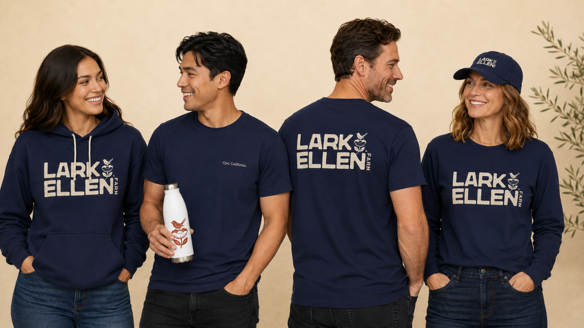 Four models wearing navy blue Lark Ellen T-shirts and a matching hoodie, standing against a light gray studio background. Two models are showing the front of the apparel, and two are showing the back, which features the brand name and logo.