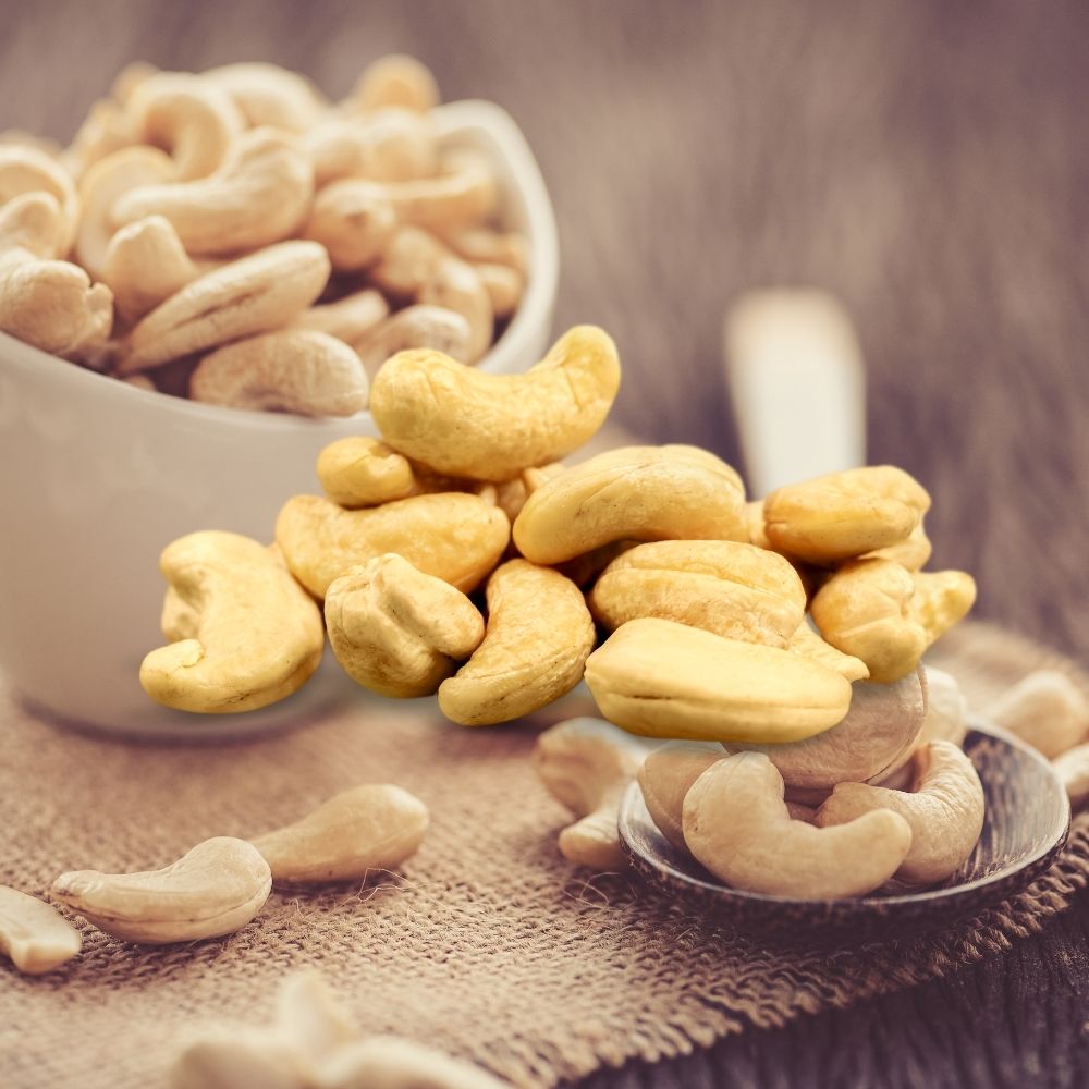 Raw cashew nuts in a bowl and spoon on burlap fabric, rich in nutrients and great for snacking.